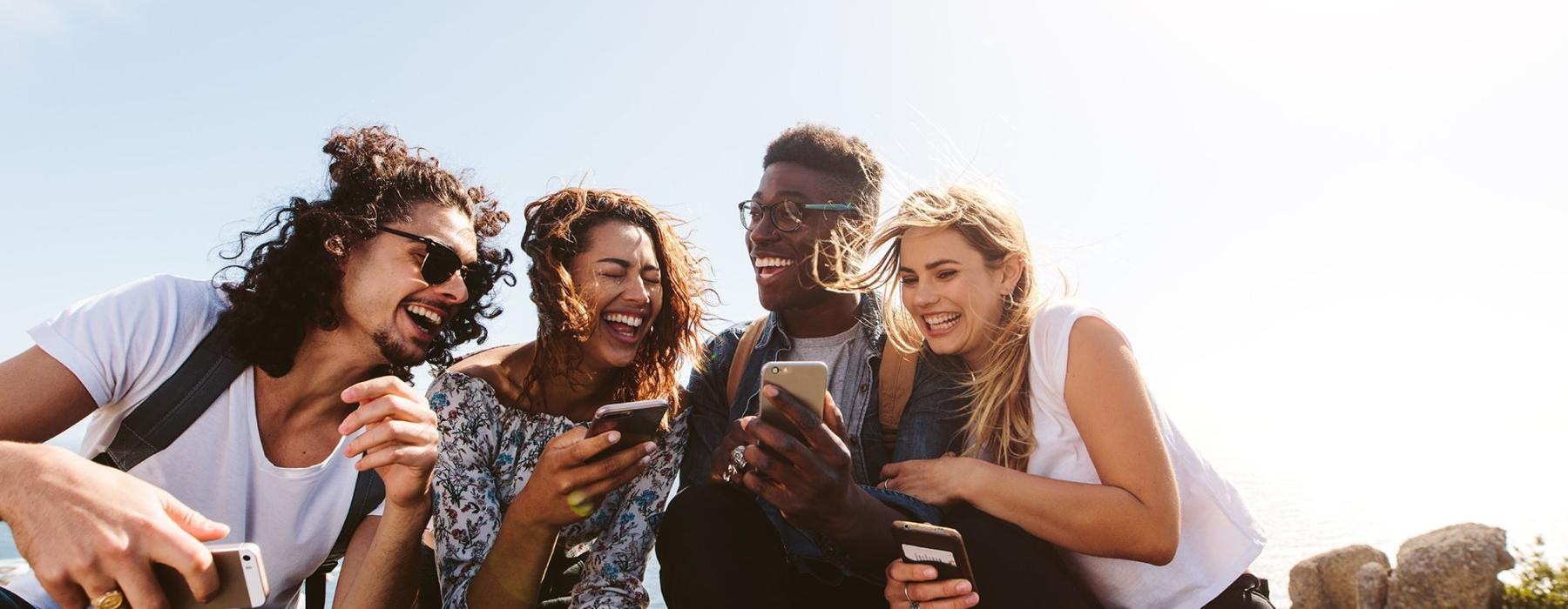 a group of friends sit outside laughing over their cell phones