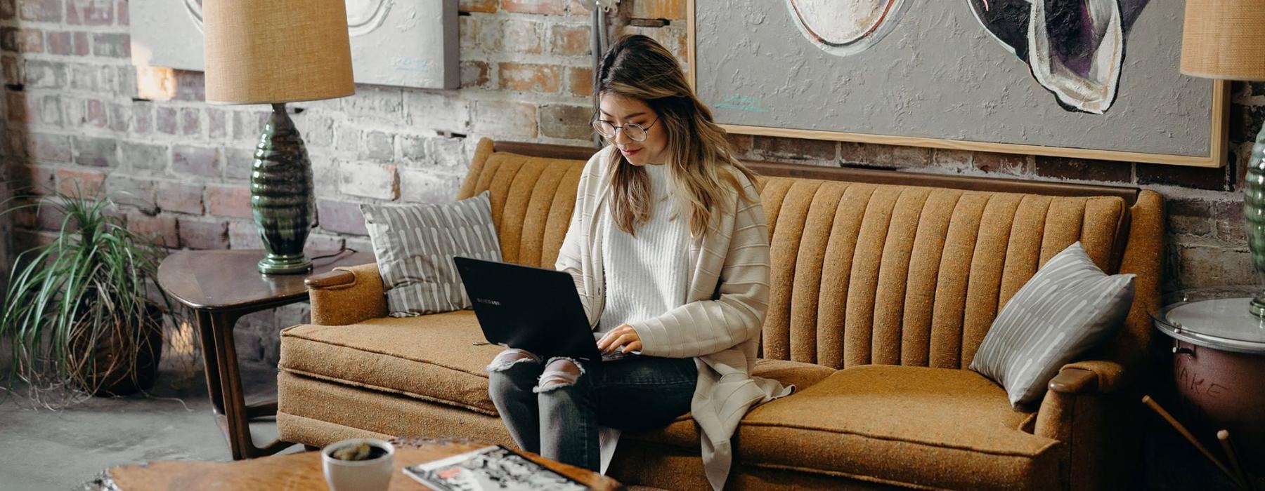 a woman sitting on a couch working on a laptop